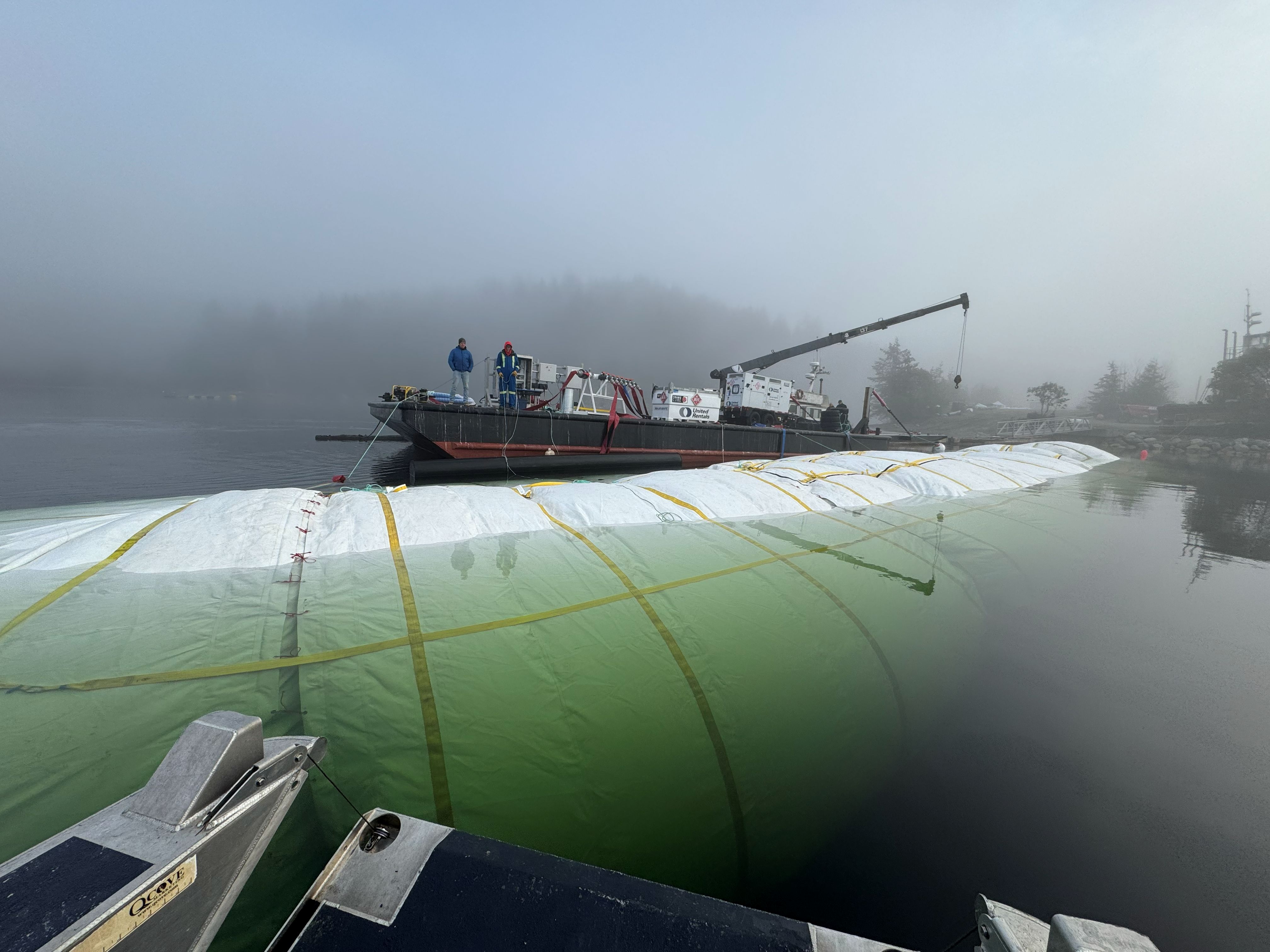 AquaLogic vessel in the water beside a work barge in foggy conditions